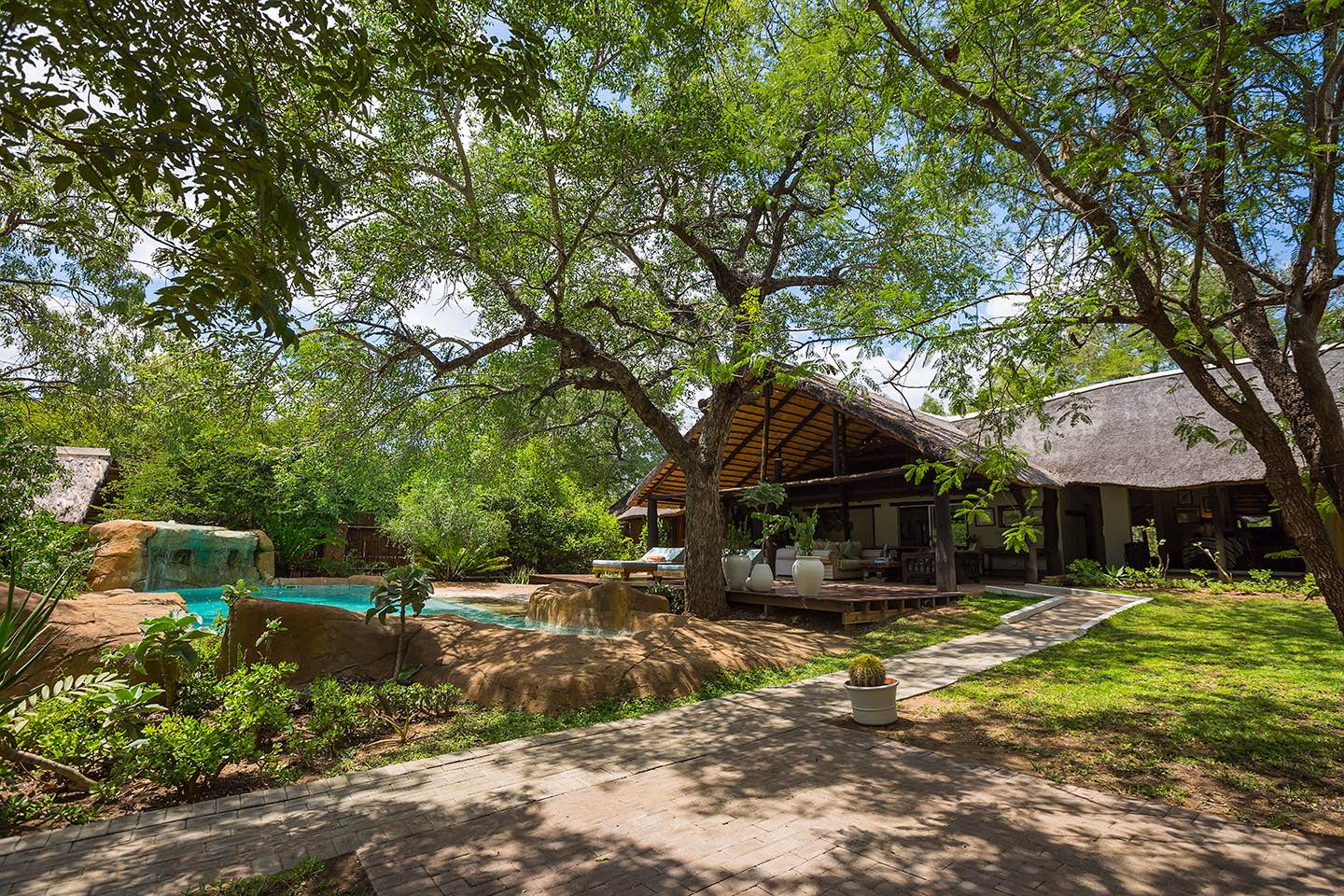 Green trees throw shade over the gardens and swimming pool on Chapungu Tented Camp