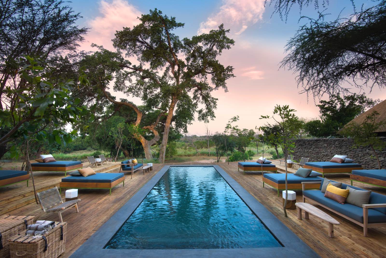 The refreshing swimming pool and stylish lounging deck surrounded by trees at Lion Sands River Lodge