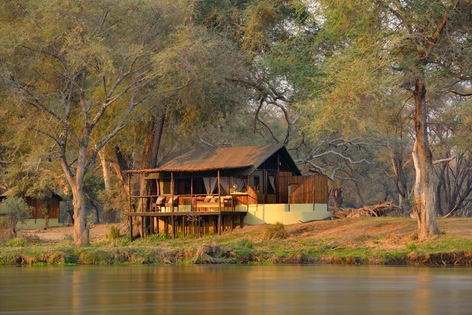 Rustic thatched chalets on the banks of the river at Old Mondoro