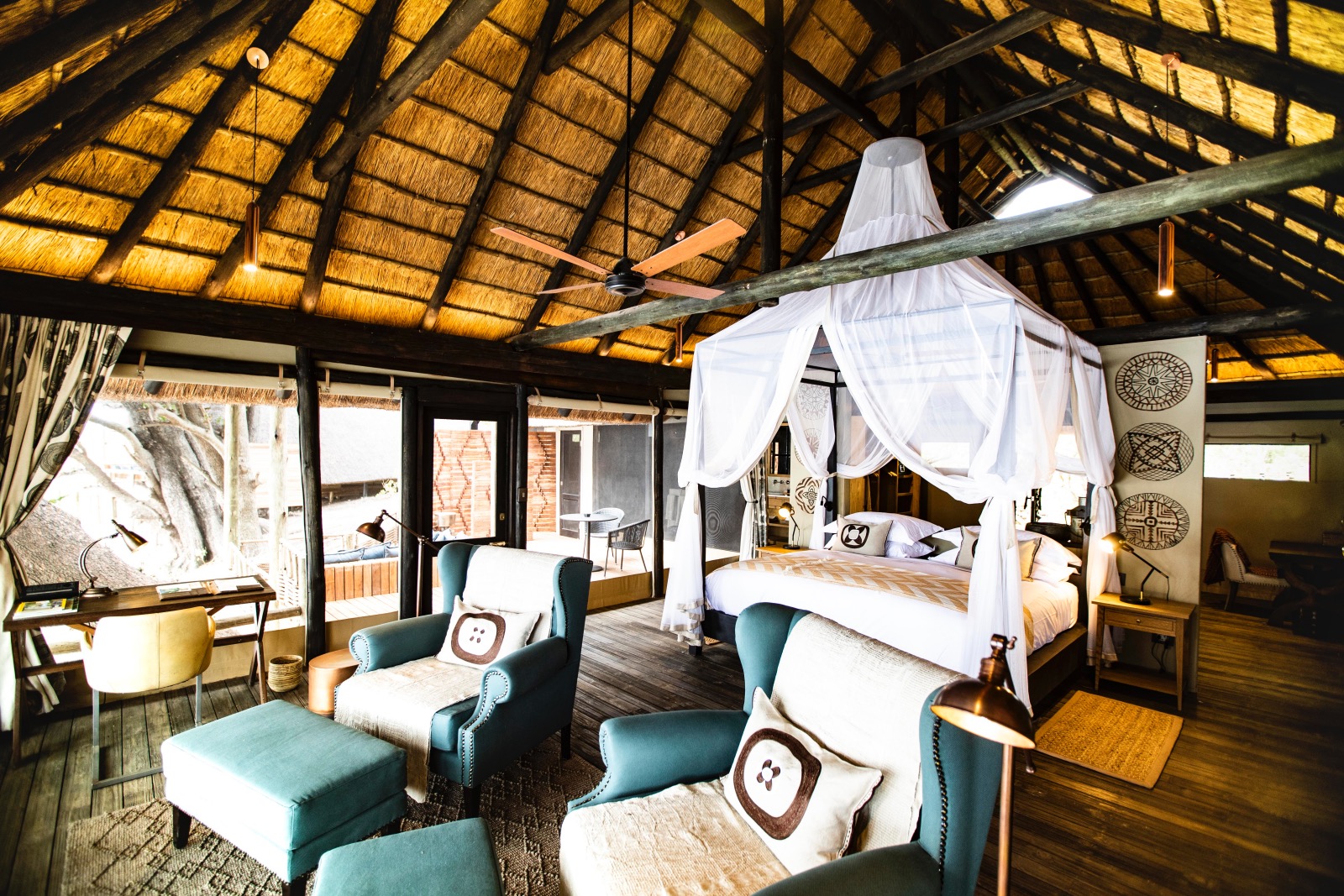 A large safari suite with high thatched ceilings and a four-poster bed in the centre and lashings of blue-green colour