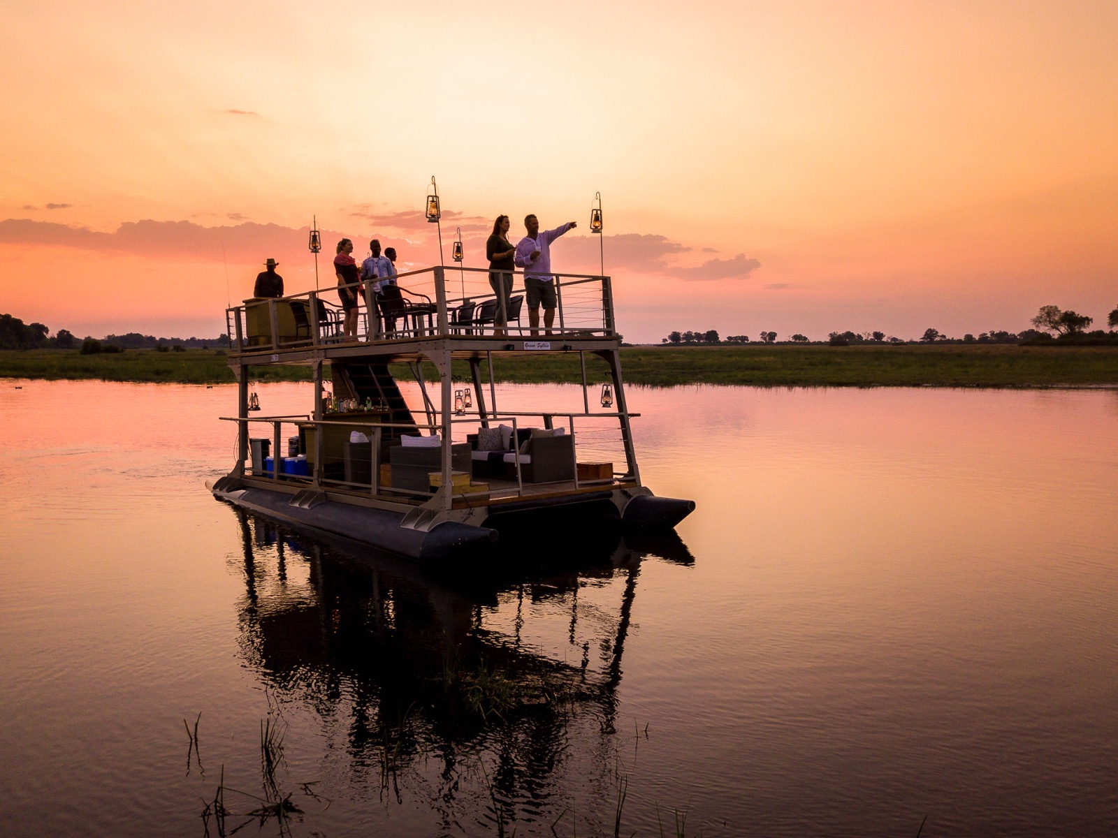 Guests toast the sunset from a boat with a bar floating across the Linyanti lagoon in Botswana