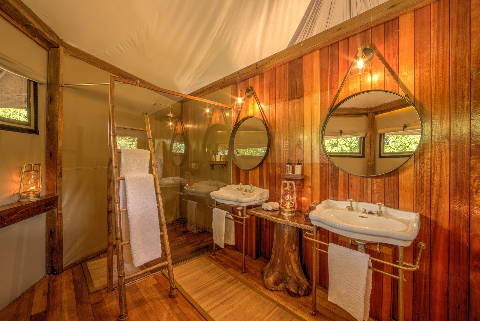En suite bathrooms with wooden panelling and canvas ceiling and twin sinks and mirrors